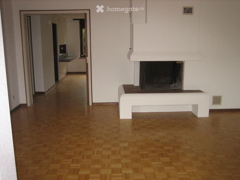 Modern living room with wooden flooring, fireplace, and a white bench in front of it. The room has white walls and a hallway leading to another area.