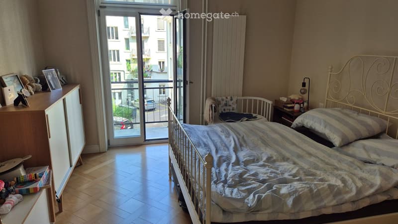 Cozy bedroom with a single bed, nightstand, radiator, and a cabinet. A balcony with a view of the street is accessible through large glass doors.