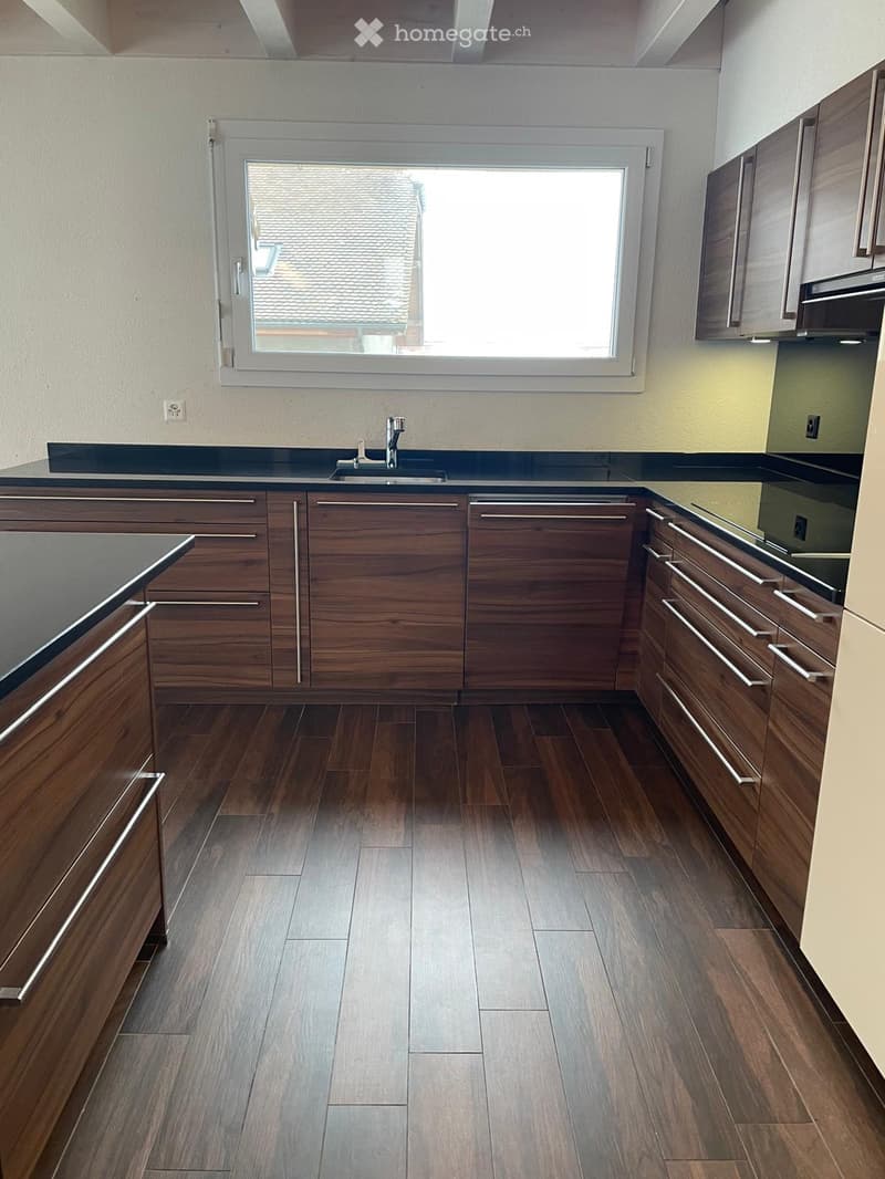 Modern kitchen with wooden cabinets, dark countertops, and a large window overlooking a roof.