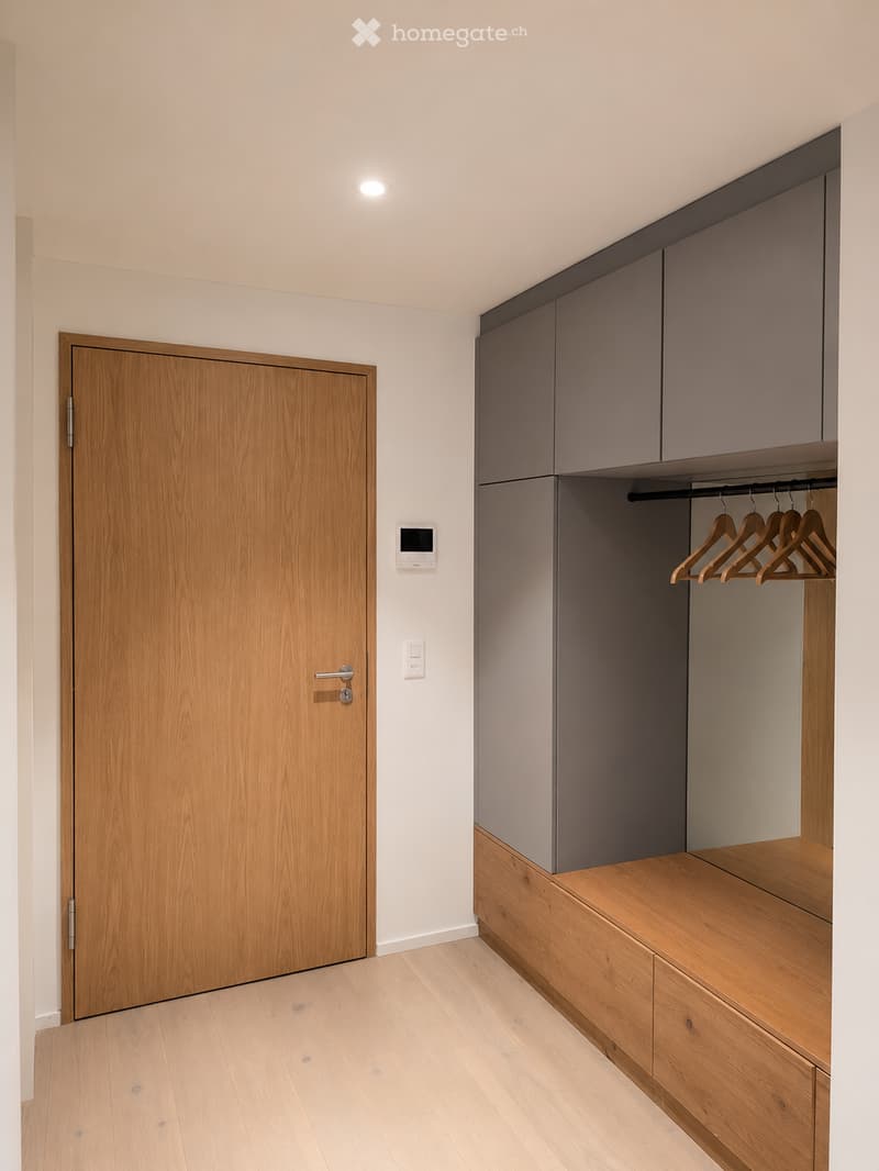 Empty room with light wooden flooring, grey built-in closet with wooden hangers, and a wooden door.