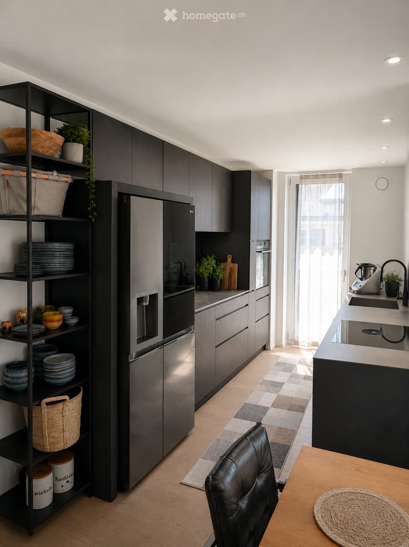 Modern kitchen with dark grey cabinets, stainless steel appliances, and a black shelving unit holding dishes and decorative items. The space features a central island with a sink and faucet, a wooden dining table with a black leather chair, and a patterne