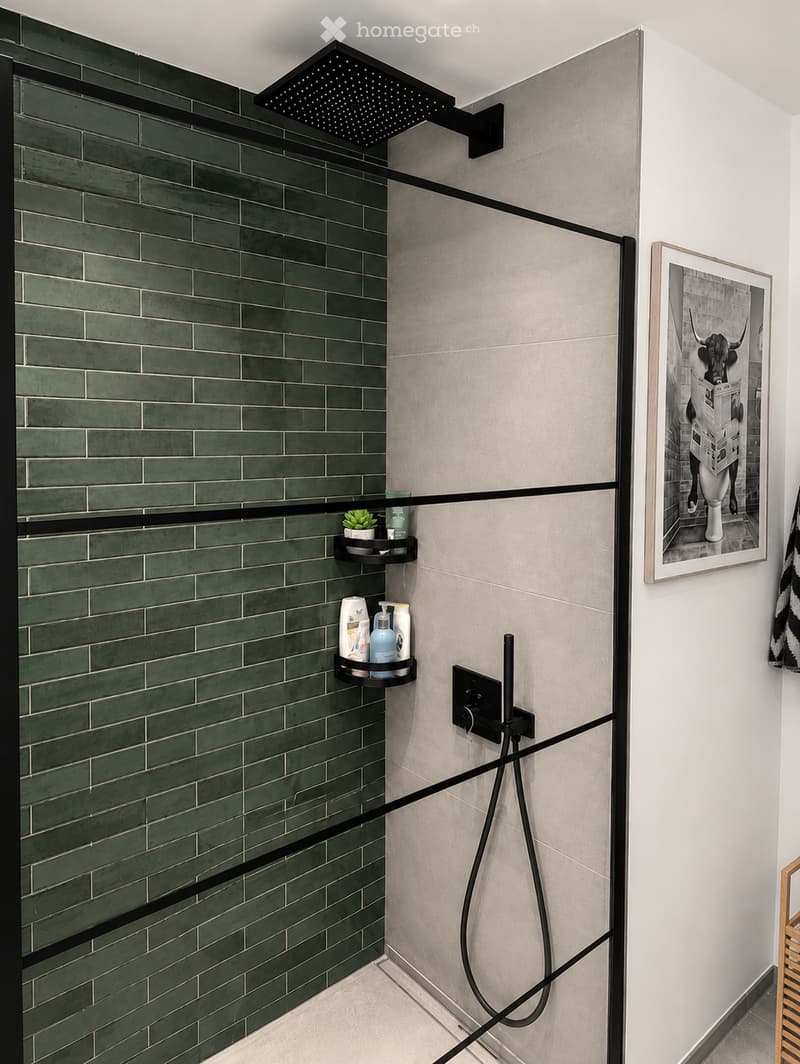 Modern shower area with green tiles, a large shower head, built-in shelves holding toiletries, and a framed picture on the wall.