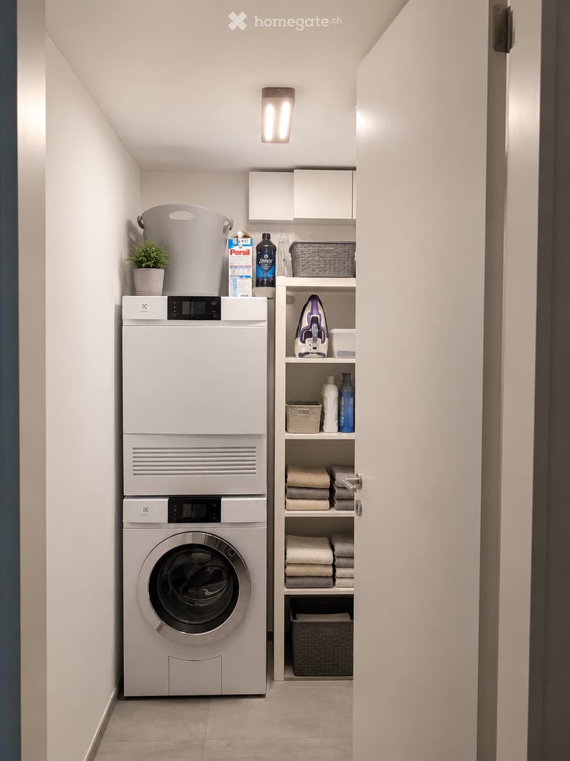 Modern, compact laundry area with a stacked washer/dryer unit, built-in shelving, and neatly organized cleaning supplies.