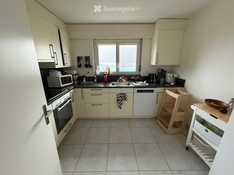 Bright kitchen with white cabinets, black countertops, and stainless steel appliances. Features include a microwave, oven, sink, dishwasher, and a small wooden cart with wheels.