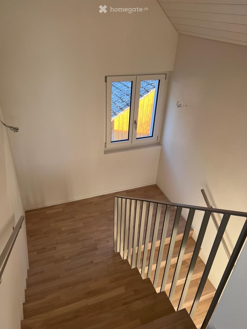 Staircase with wooden steps, metal railing, and a window overlooking a roof area.