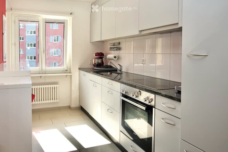 Modern kitchen with white cabinets, stainless steel appliances, granite countertops, and a window view of a cityscape.