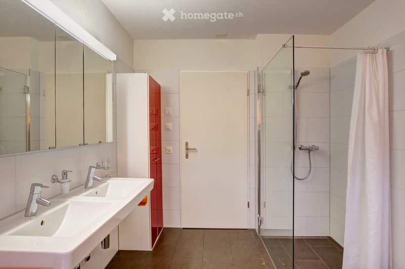 Modern bathroom with a double sink, large mirror, glass-enclosed shower, and a white tiled design.