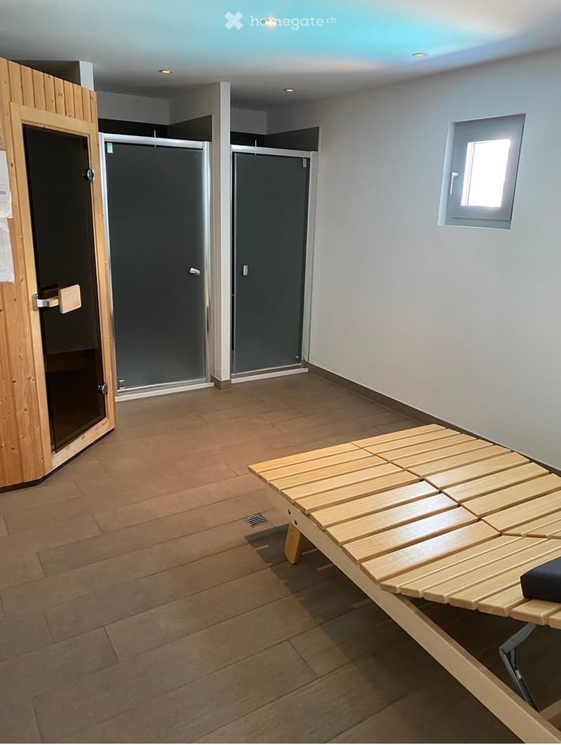 Empty room with wooden flooring, two glass shower enclosures, a small window, and a wooden bench.