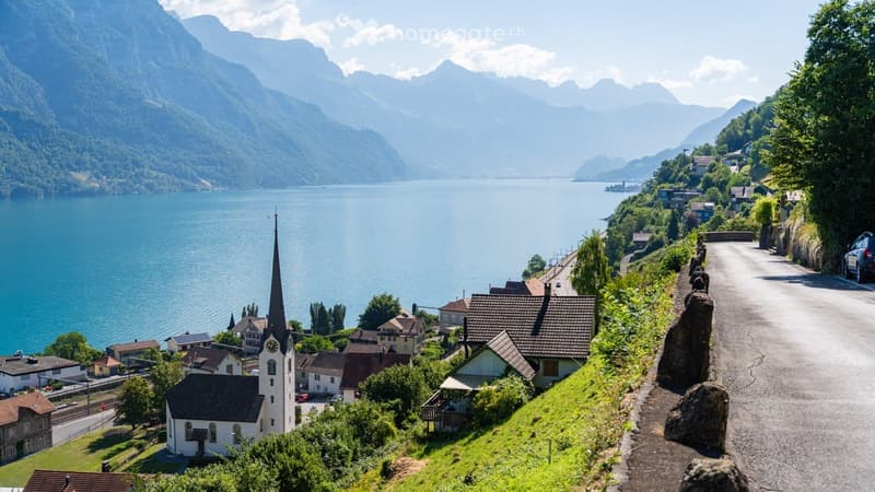 Scenic view of a lakeside village with traditional houses, a church tower, and surrounding mountains.