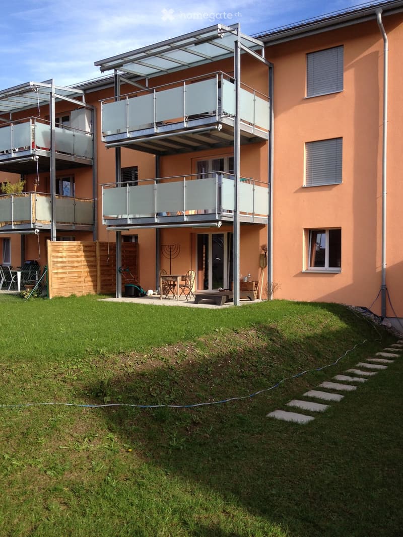 Modern house with raised ground floor, multiple balconies, and a well-maintained lawn.
