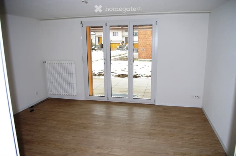 Empty room with wooden flooring, white walls, and large sliding glass doors leading to an outdoor area.