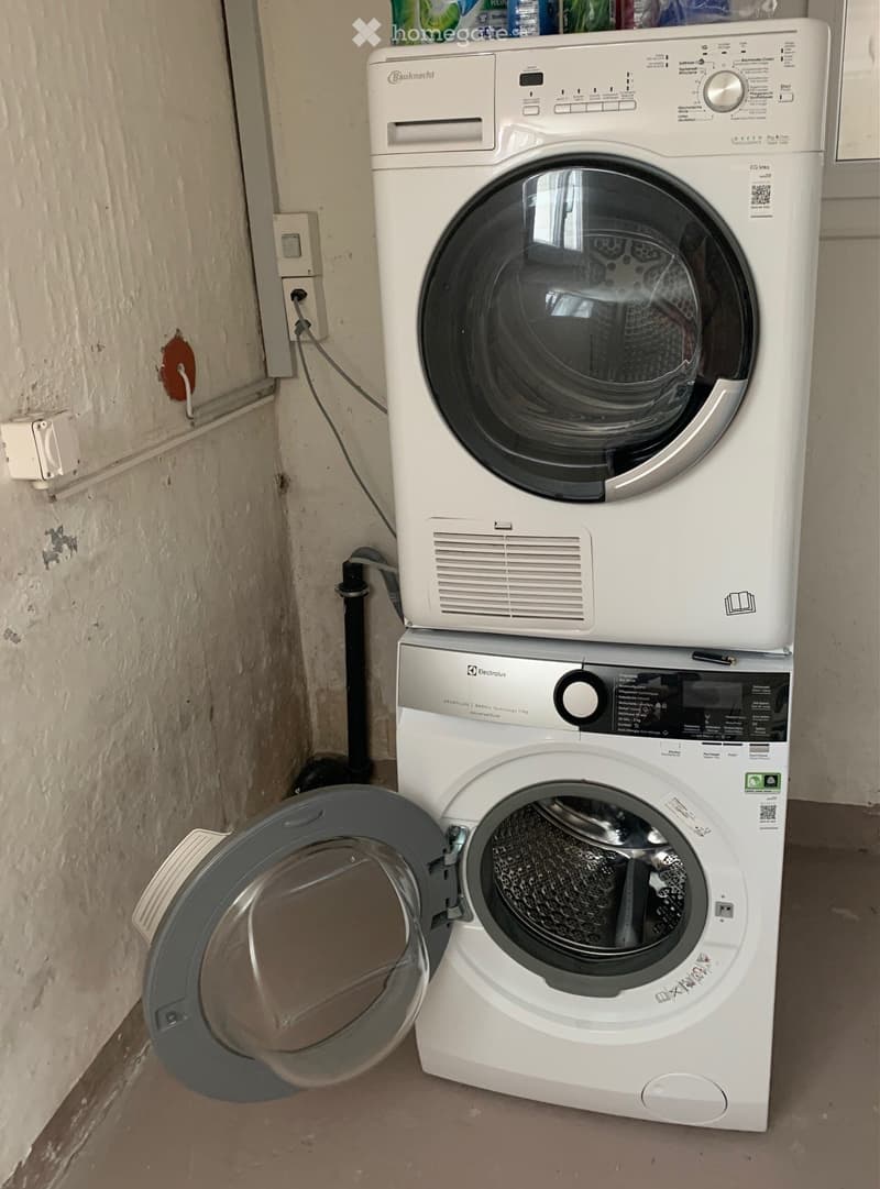 A compact bathroom with a stacked washing machine and dryer unit, both white with control panels and transparent doors.