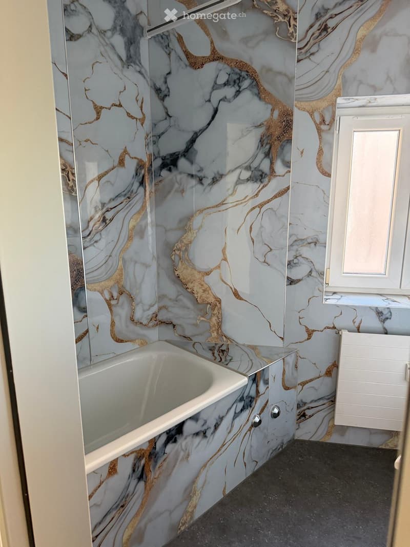 Bathroom. Modern bathroom with marble-effect walls in grey and gold, a bathtub with a glass shower enclosure, and a white cabinet.