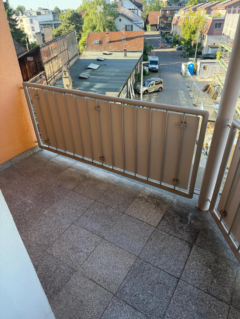 Balcony / Terrace. Balcony with tiled floor and metal railing, overlooking a street with parked cars and buildings.