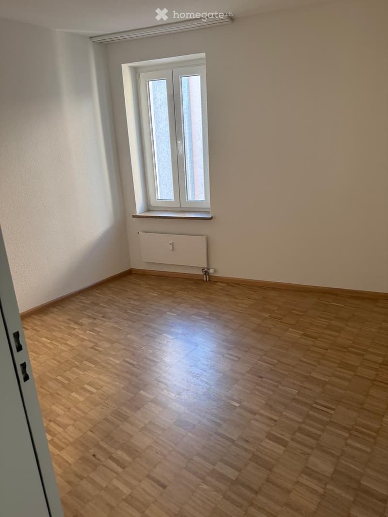 Unfurnished Room. Empty room with wooden flooring, white walls, a window with frosted glass, and a radiator below the window.