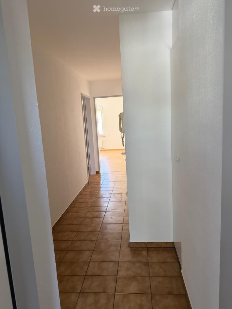 Corridor / Hallway. Empty hallway with tiled floor and white walls, featuring a door leading to another room.