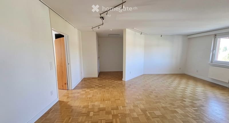Empty room with wooden parquet flooring, white walls, and large windows allowing natural light. No furniture or equipment present.