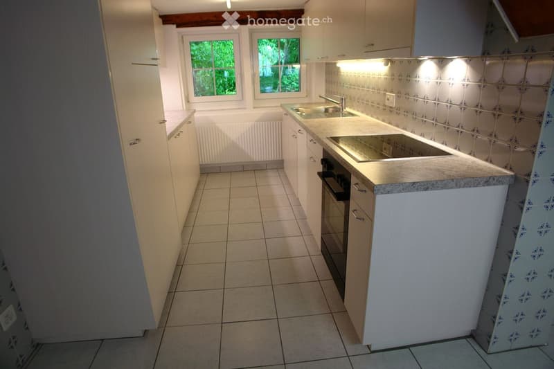 Modern kitchen with white cabinets, granite countertop, sink, and built-in oven. Light-colored tiled floor and walls with decorative tiles.