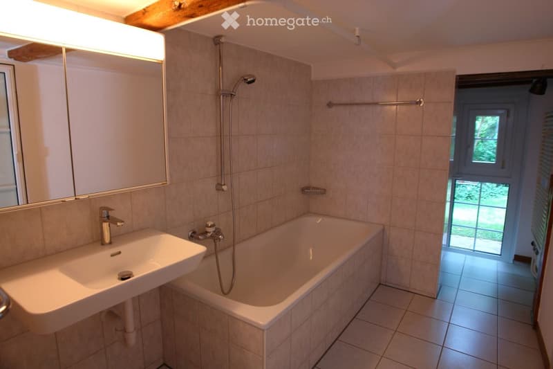 Modern bathroom with a white sink, bathtub, and large mirror. Features a showerhead and tiled walls.