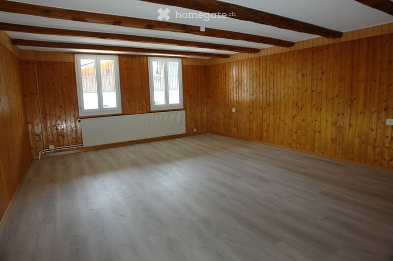 Empty room with wooden walls, wooden floor, and two windows. Exposed wooden beams on the ceiling.