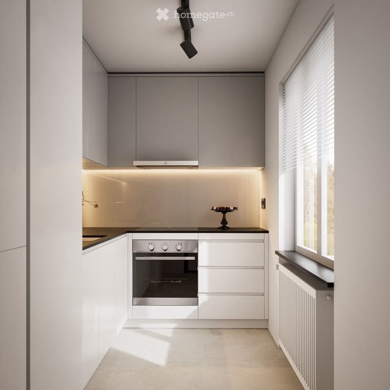 Modern kitchen with sleek white cabinets, stainless steel oven, and built-in lighting. Features a large window with blinds and a small decorative cake on the counter.