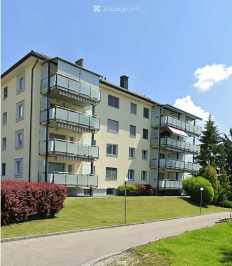Multi-story residential building with multiple balconies and a well-maintained lawn in front.