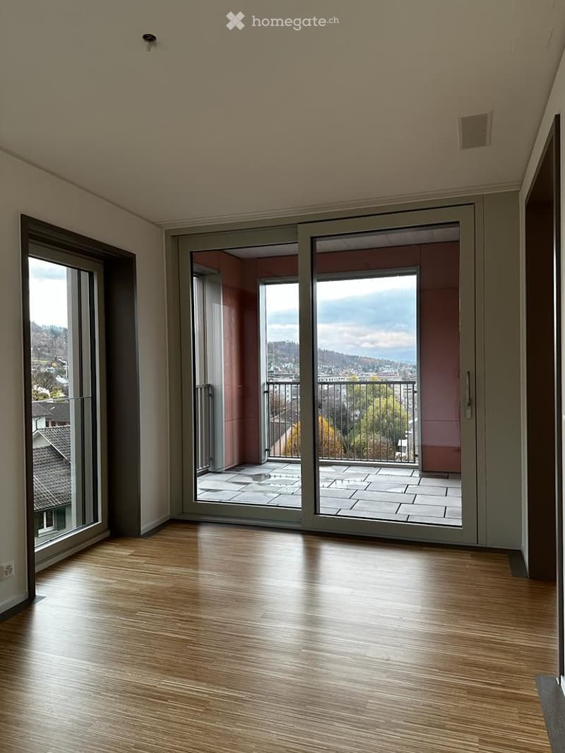 Empty room with wooden flooring, large sliding glass doors leading to a balcony with a scenic view of the landscape.