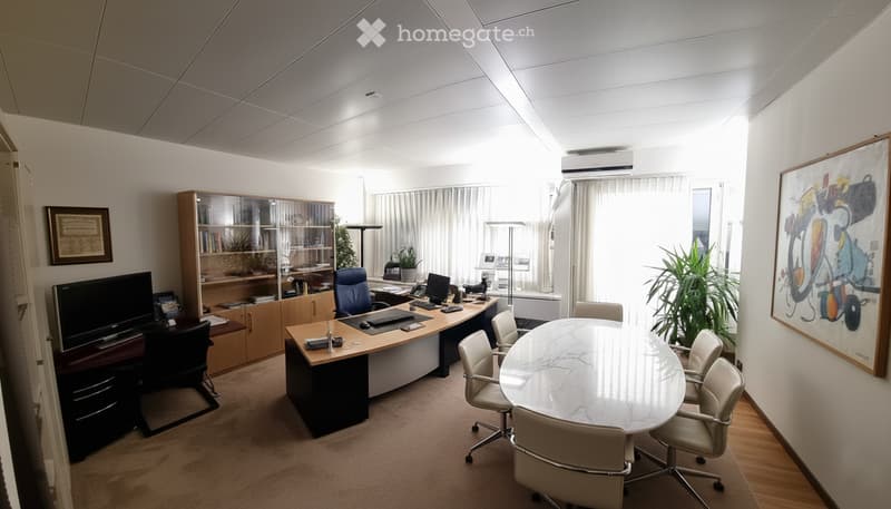 Office space with a large desk, multiple chairs, a round meeting table, a cabinet, and artwork on the walls.