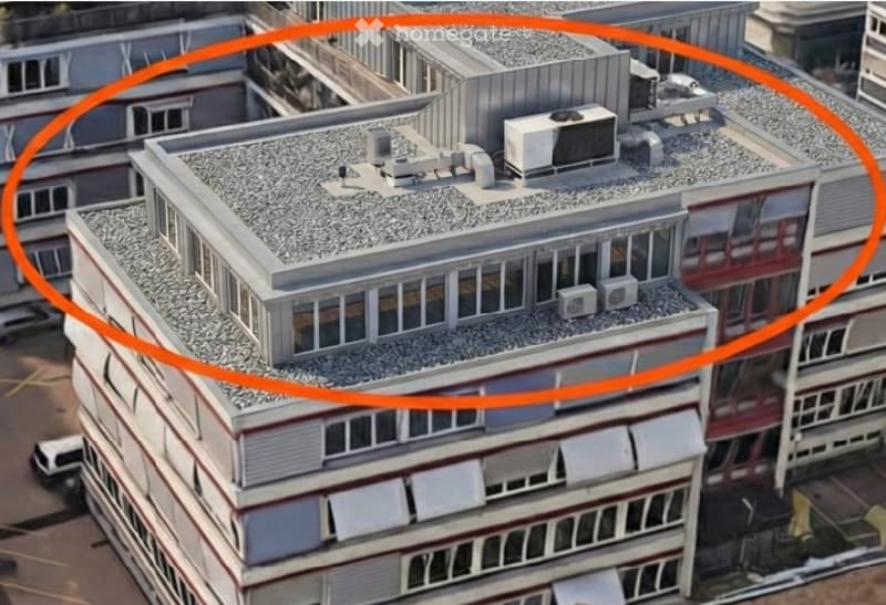 A multi-story building with a flat roof, visible air conditioning units, and surrounding structures.