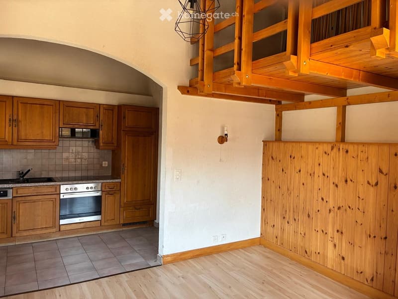 A modern kitchen with wooden cabinets, stainless steel appliances, and a wooden loft area above.