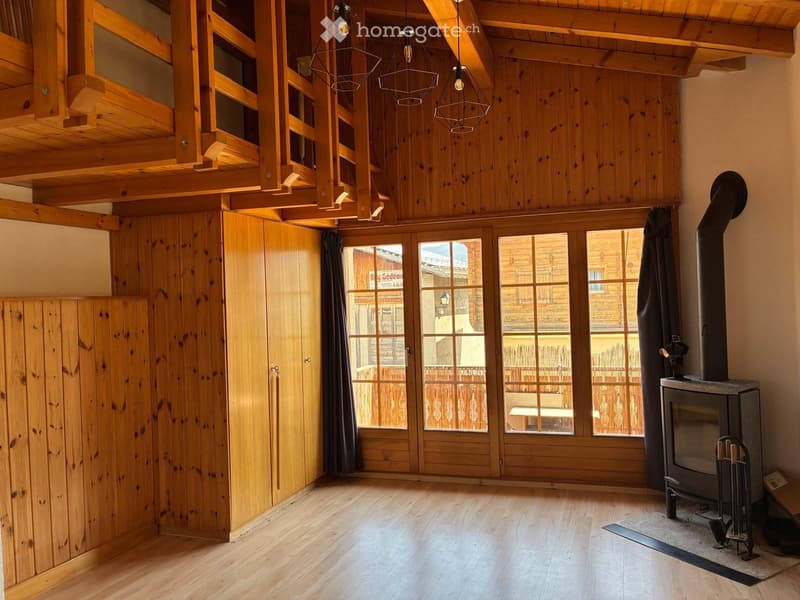 Cozy living room with wooden walls, exposed wooden beams, large windows, and a fireplace.