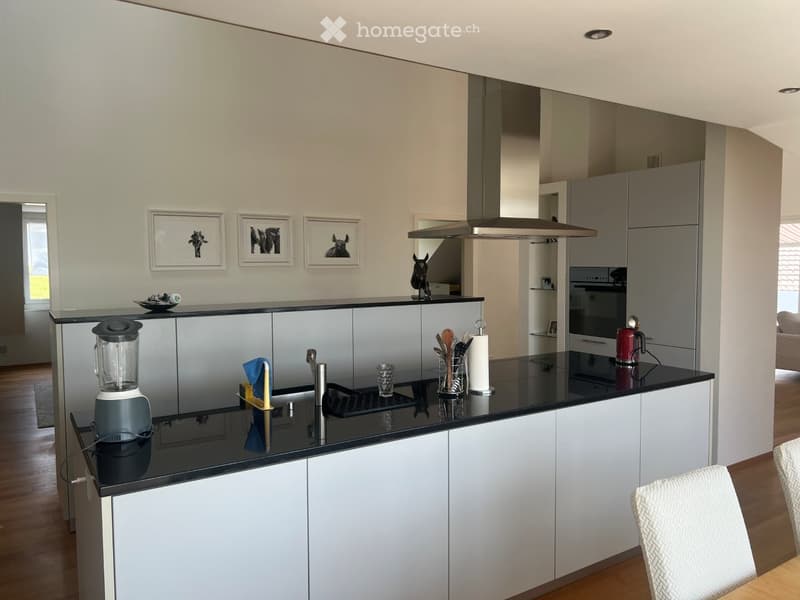 Modern kitchen with white cabinets, black countertops, stainless steel appliances, and a central island. Features include a blender, a range hood, and a sink with a faucet.