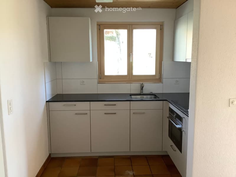 Modern kitchen with light-colored cabinets, a black countertop, a sink, and an oven. The room has tiled flooring and a window above the sink.