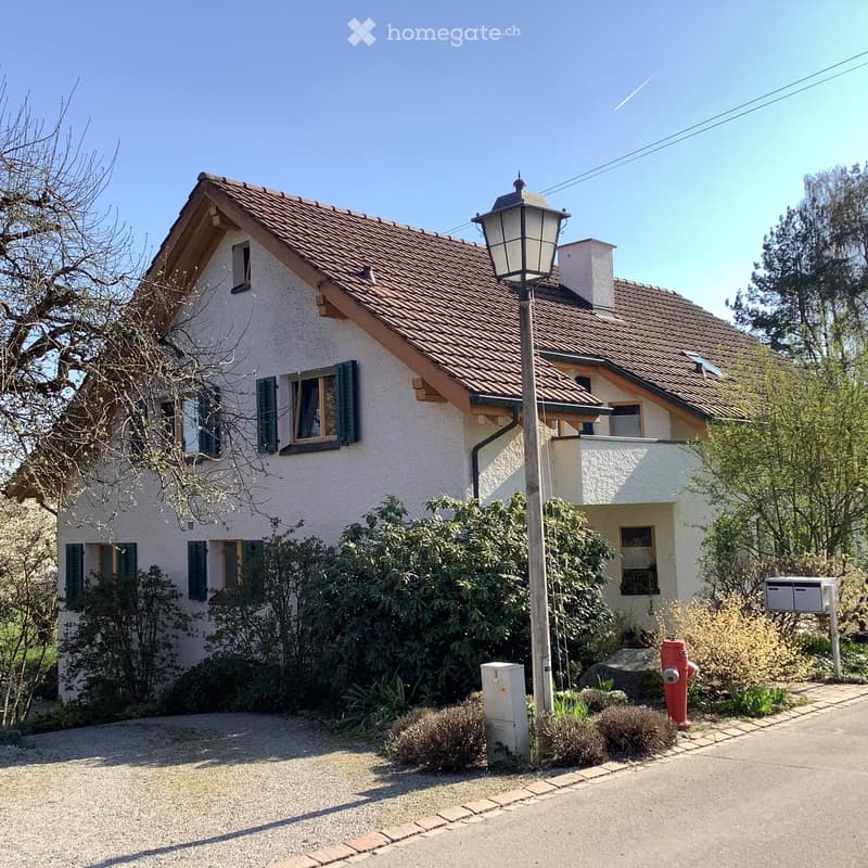 Two-story house with a tiled roof, white exterior, green shutters, and a small garden area.