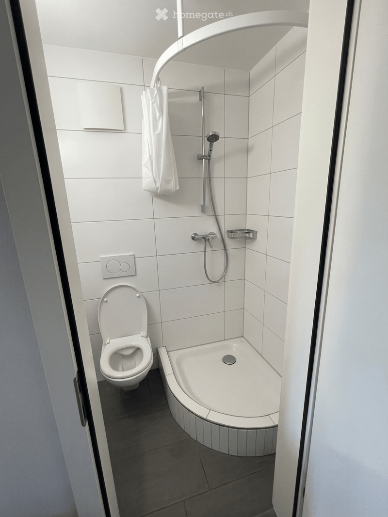 Modern bathroom with white tiles, a toilet, a bathtub, a showerhead, and a towel hanging on the wall.
