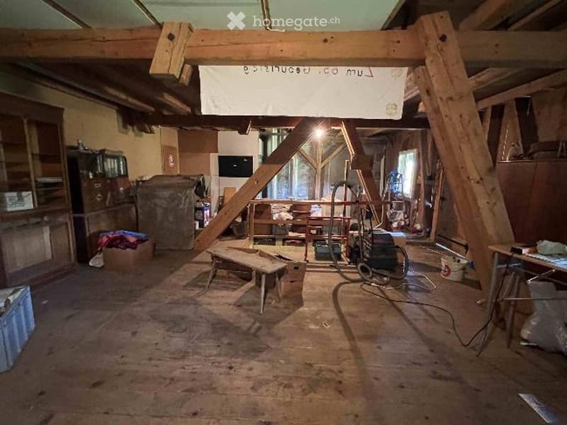 Empty attic space with exposed wooden beams, wooden floor, and some construction materials and tools scattered around.