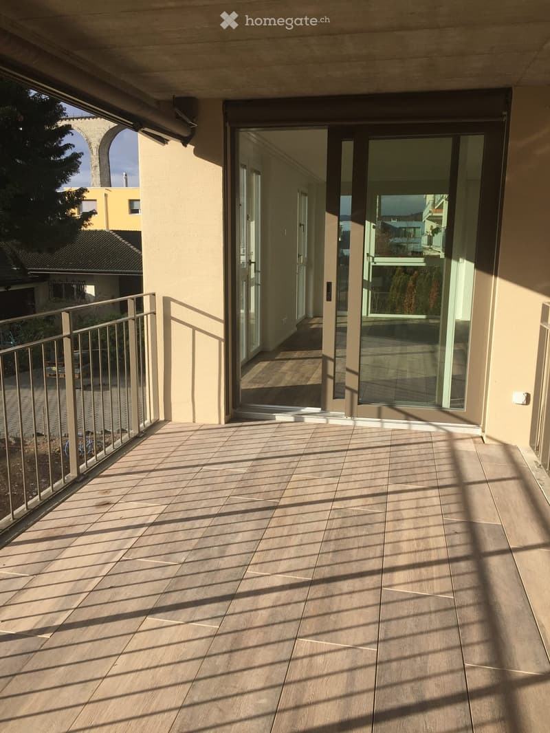 Balcony with tiled floor, metal railing, and glass doors leading to an interior space.