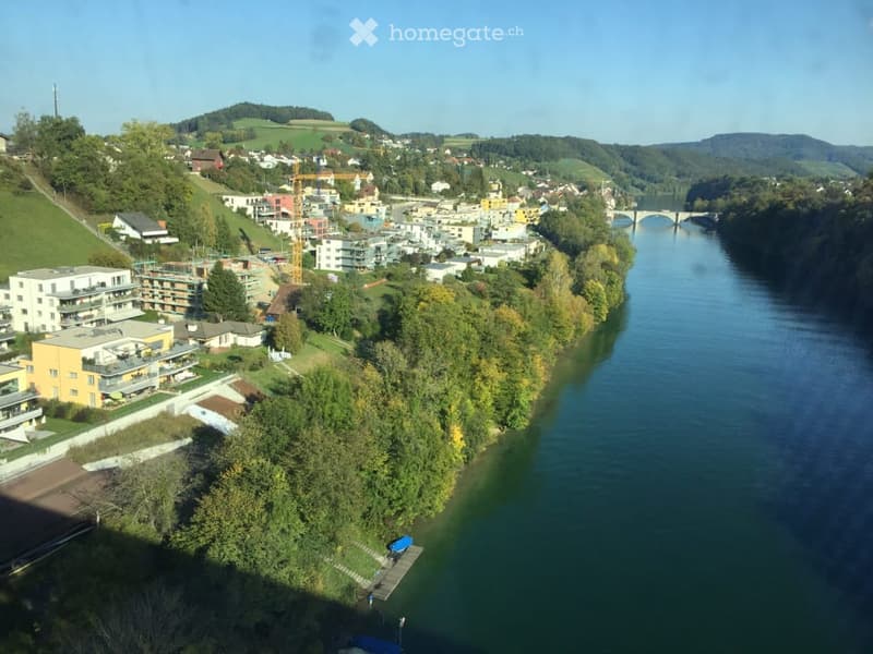 Aerial view of a town with residential buildings, a river, and surrounding greenery.