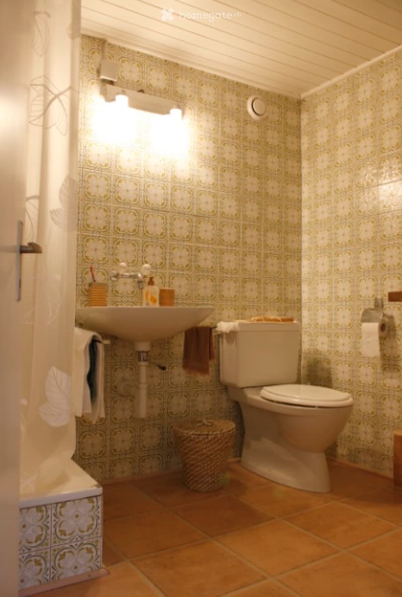 Bathroom with floral patterned wallpaper, a sink with a faucet, a toilet, a towel, and a wicker basket on the floor.