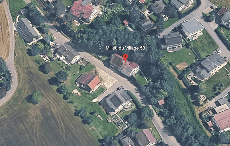Aerial view of a residential area with multiple houses, surrounded by greenery and roads.