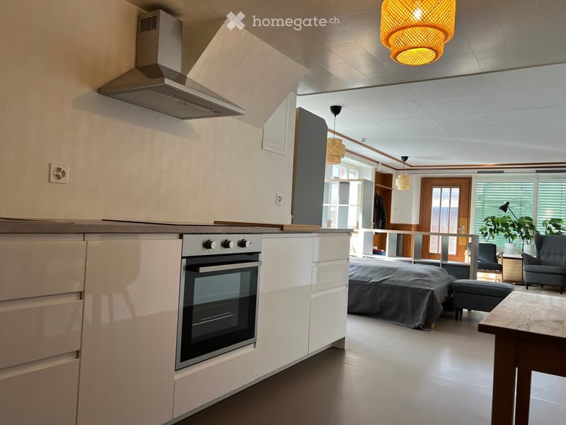 kitchen with oven, modern lighting, white cabinetry, stainless steel appliances, open bedroom layout, gray covered bed, wooden table