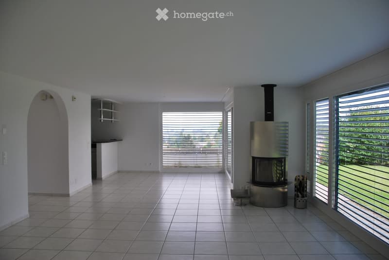 Bright, spacious living room with tiled floor, large windows, and a modern metal fireplace.