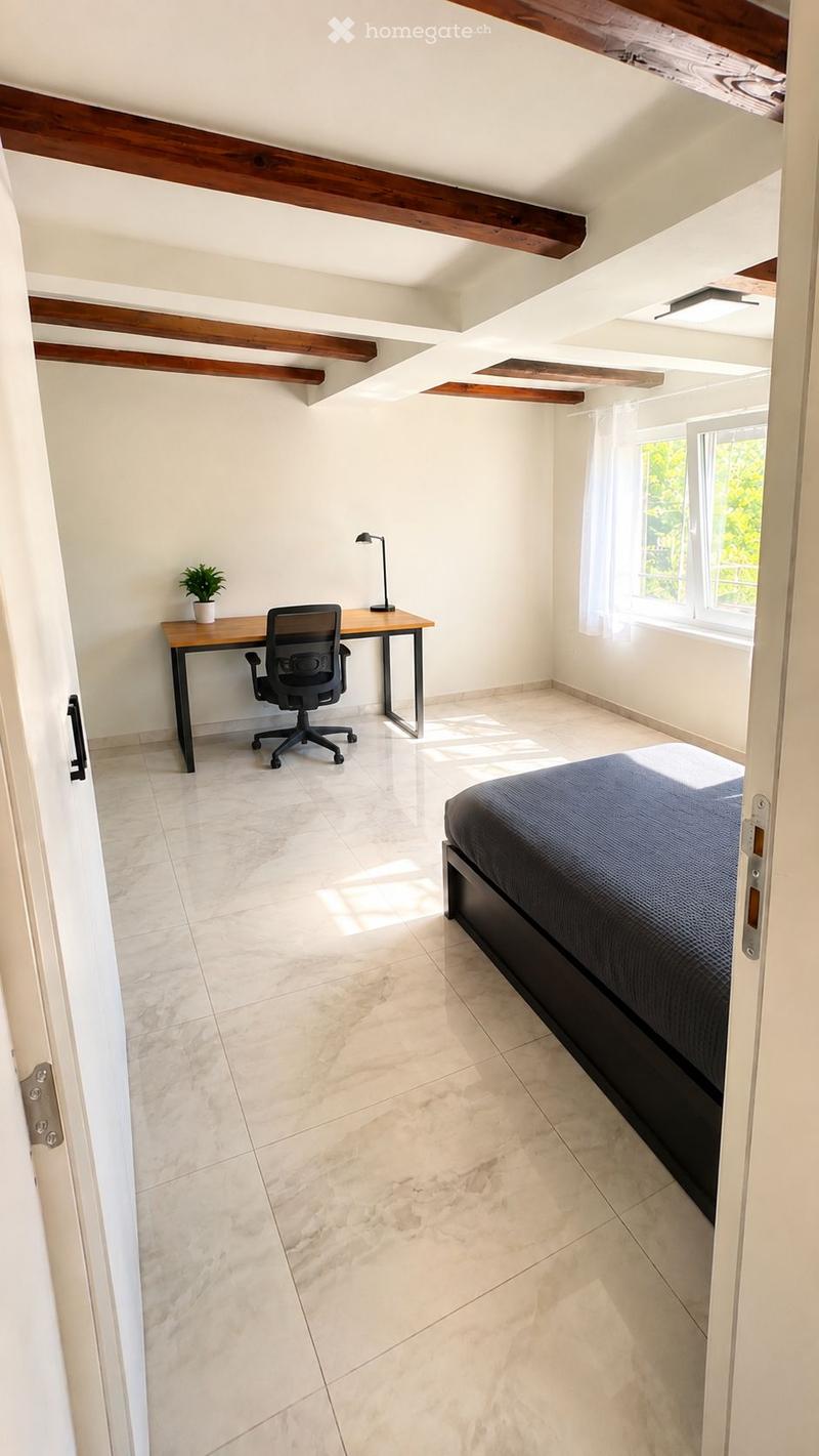 Bright bedroom with exposed wooden beams, marble flooring, a bed with dark bedding, a desk with a chair, a small plant, and a lamp.