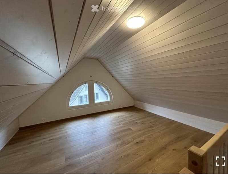 Empty attic room with wooden walls and floor, skylight window, and exposed wooden beams on the ceiling.