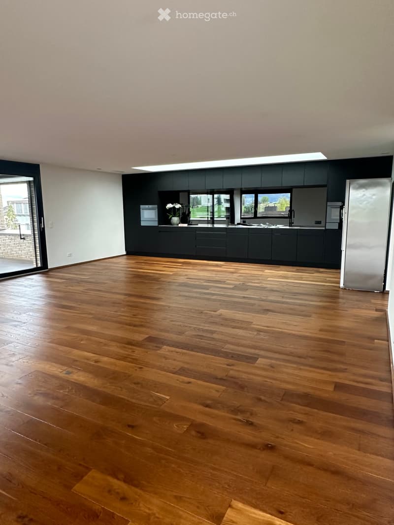 Empty kitchen with dark grey cabinets, stainless steel appliances, and wooden flooring.