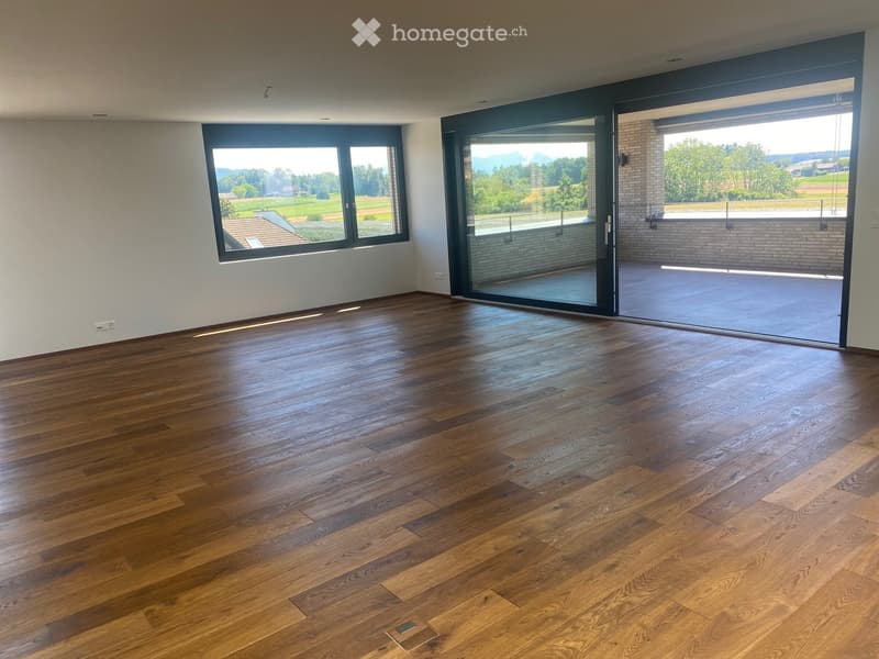 Empty room with wooden flooring, large windows, and sliding glass doors leading to a balcony or terrace.