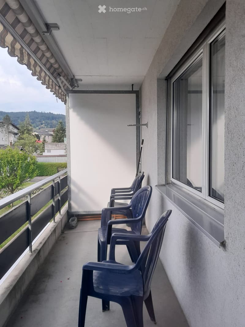 Balcony with several blue plastic chairs, metal railing, and a view of greenery and houses.