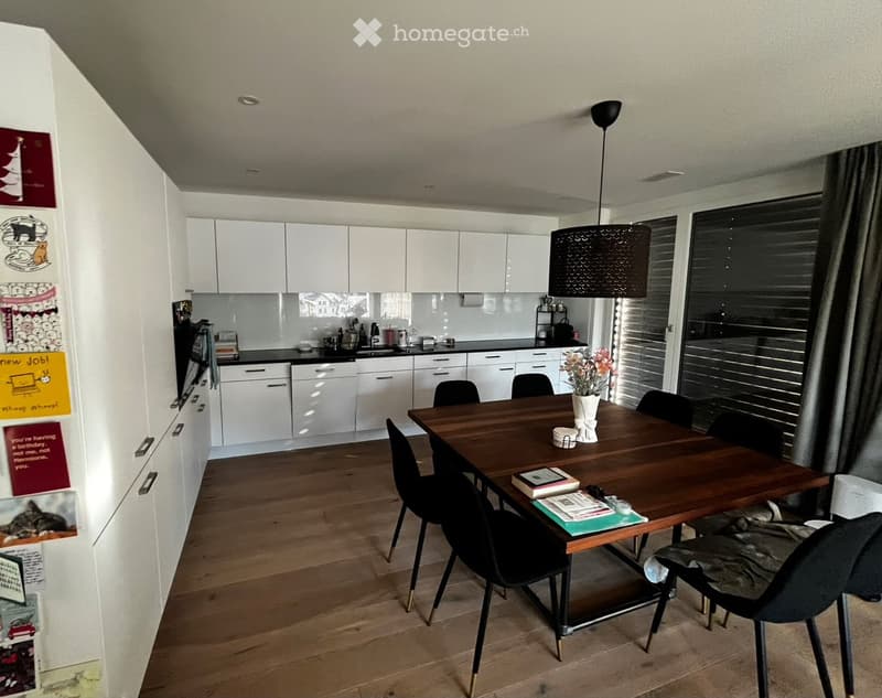 Modern kitchen and dining area with white cabinets, wooden floor, large window with blinds, and a dining table with chairs.