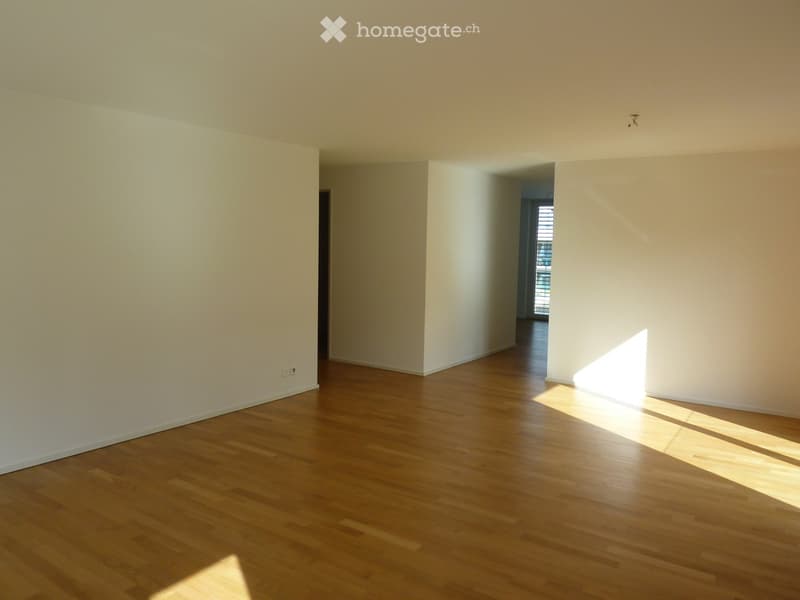 Empty room with light wooden flooring and white walls, featuring natural light streaming in from a window in the adjacent room.