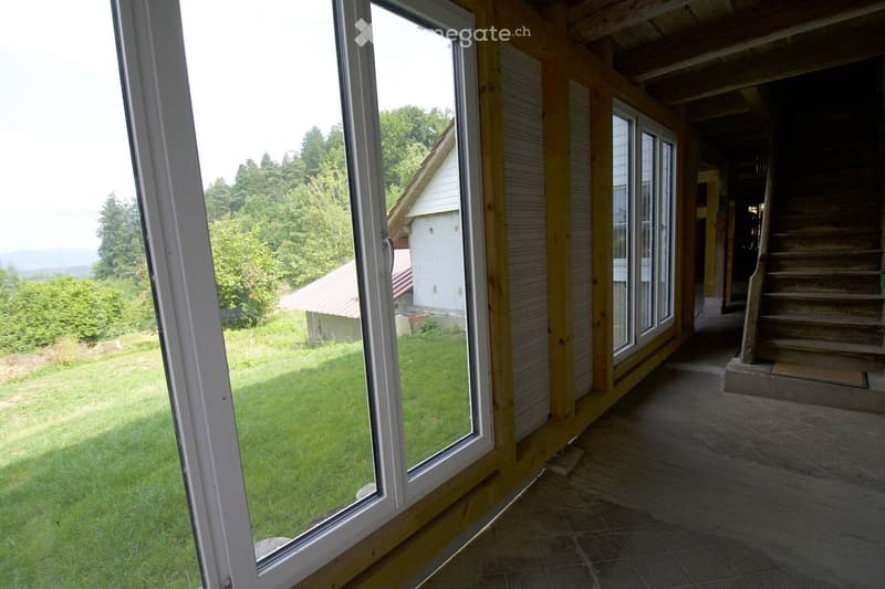 Balcony with wooden railings, tiled floor, large windows overlooking a grassy yard and trees.